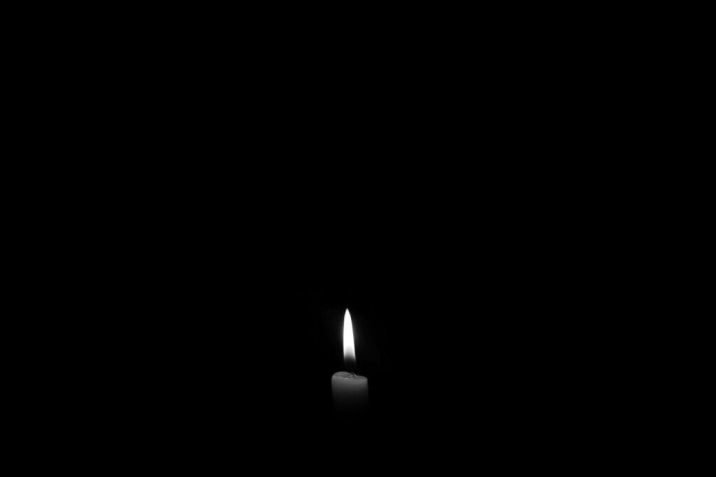 Minimalist grey candle with flickering flame on black background symbolizing hope and resilience Wallpaper