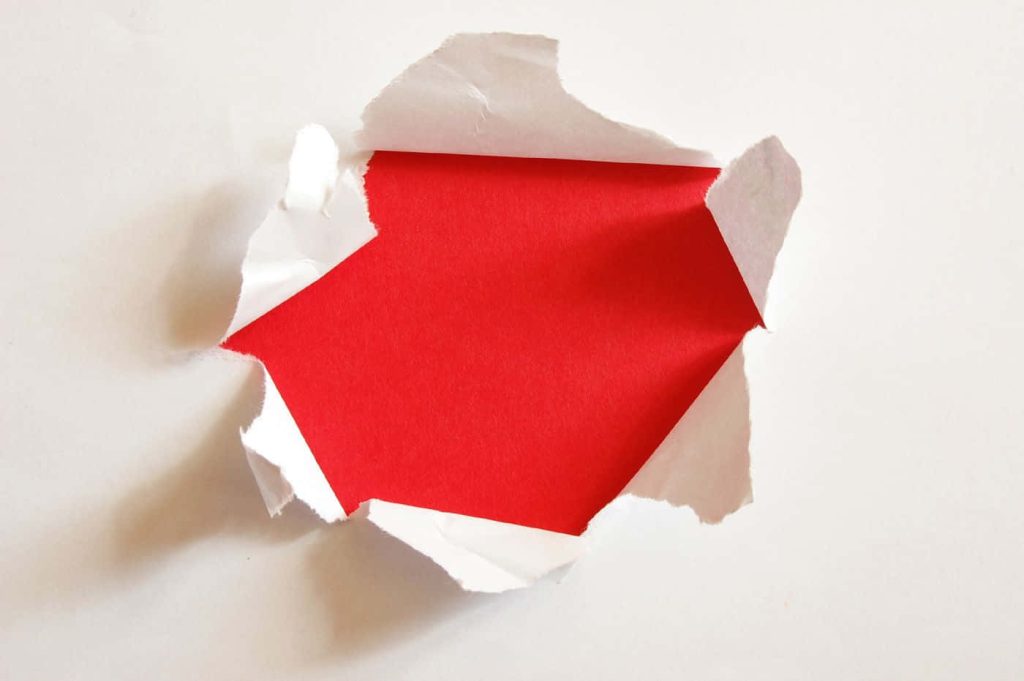 Minimalist wallpaper a jagged torn white paper peel revealing solid red background close up