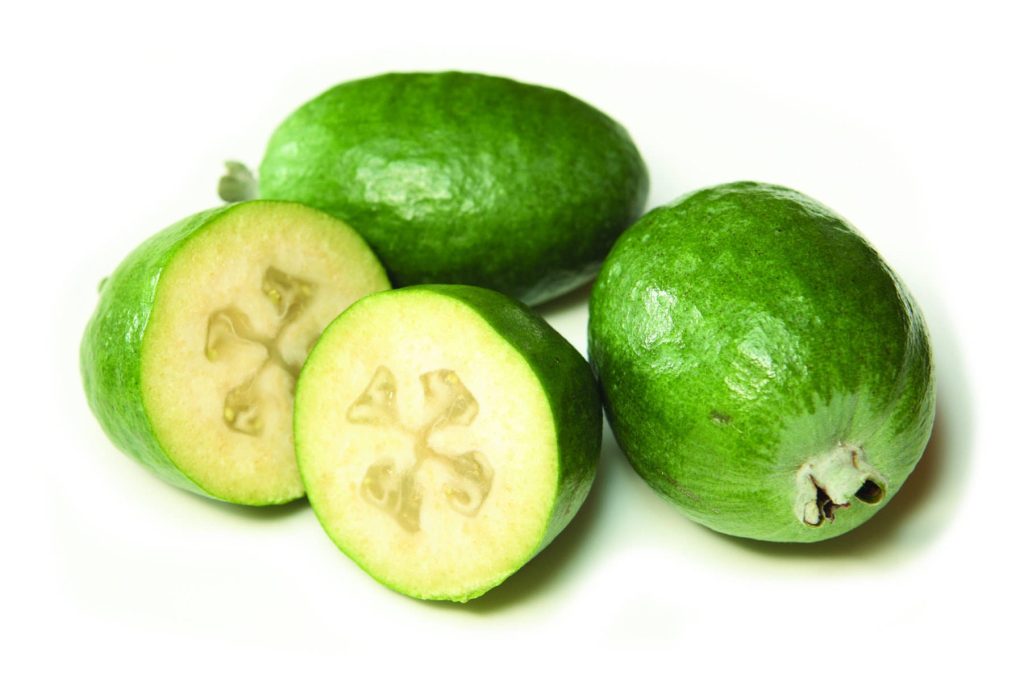 Minimalist wallpaper with fresh feijoas whole and sliced on clean white background studio photo