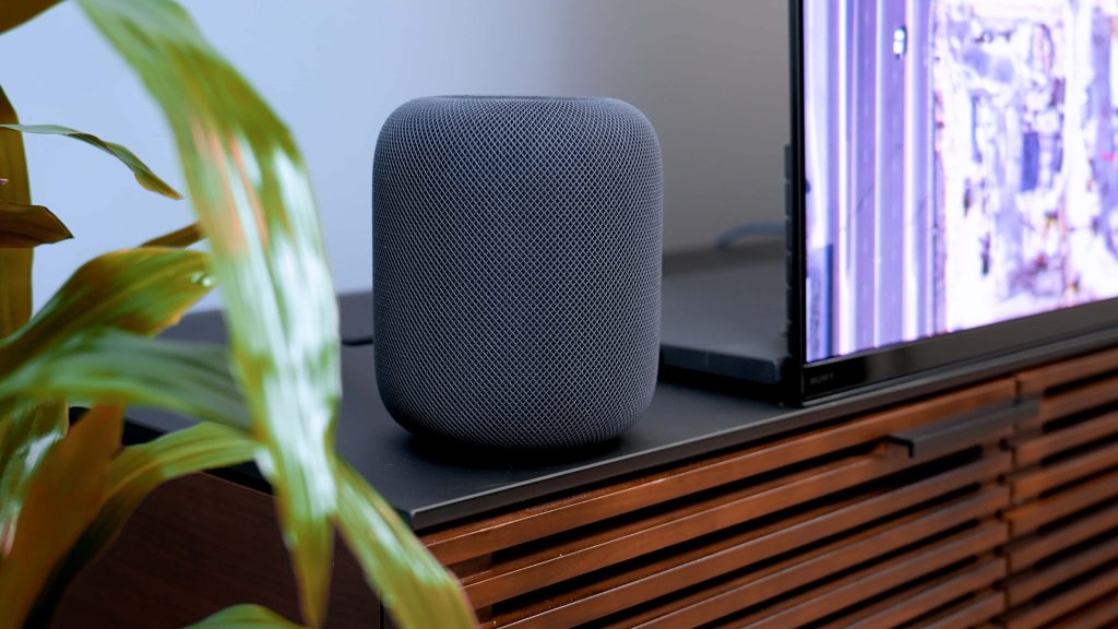 Charcoal gray Apple HomePod on wood media console with blurred plant and Sony TV background Wallpaper
