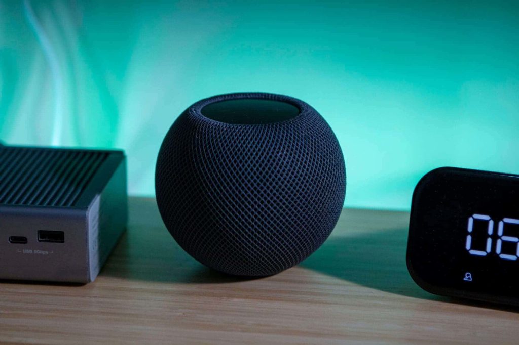 Sleek HomePod Mini with USB-C hub and digital clock on wooden desk with teal ambient light Wallpaper