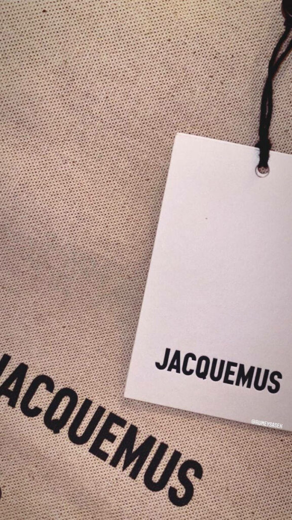 Minimalist Jacquemus wallpaper with prominent logo on textured beige background and branded tag