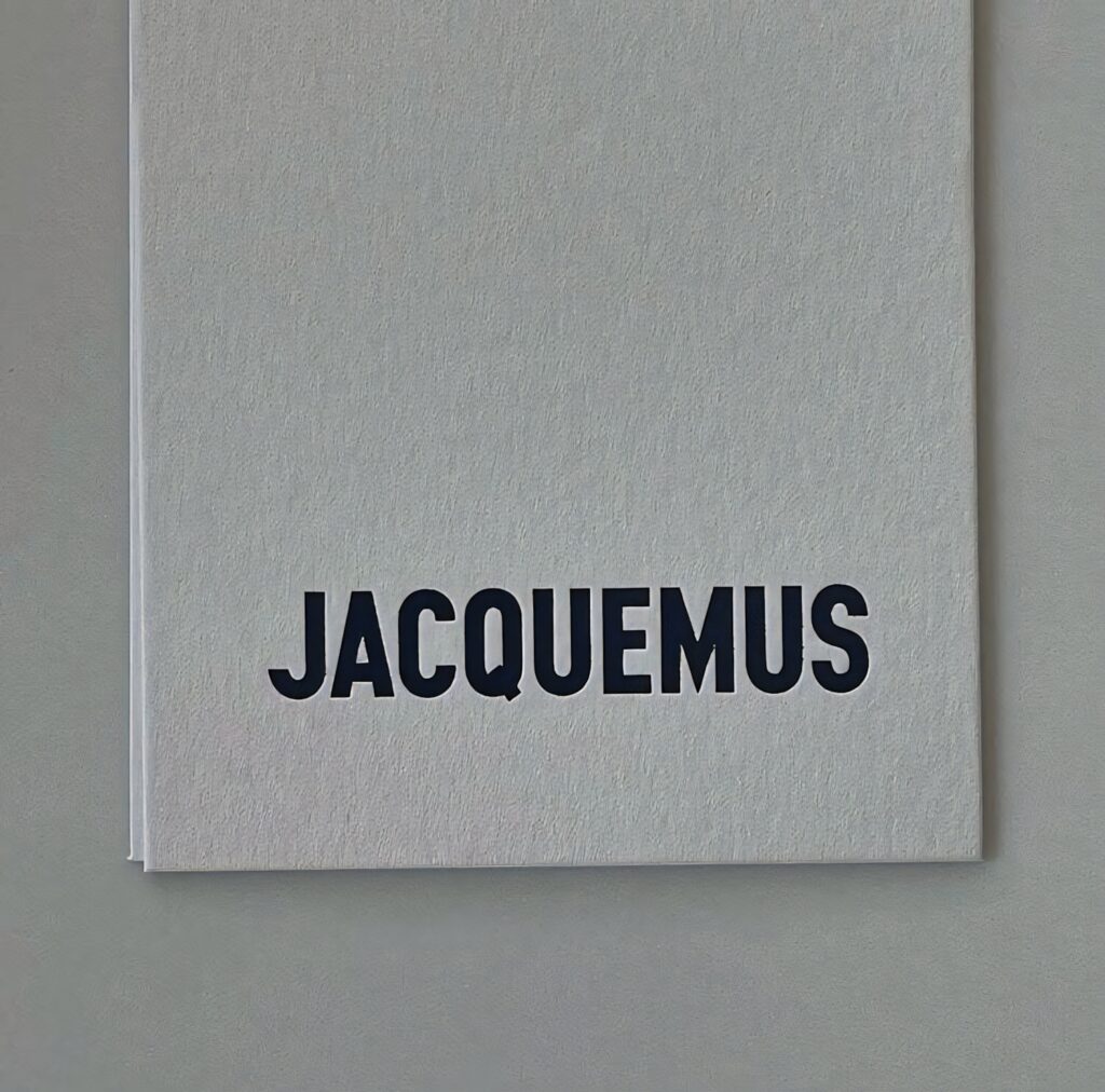 Minimalist Jacquemus logo on textured white paper background stylish wallpaper design