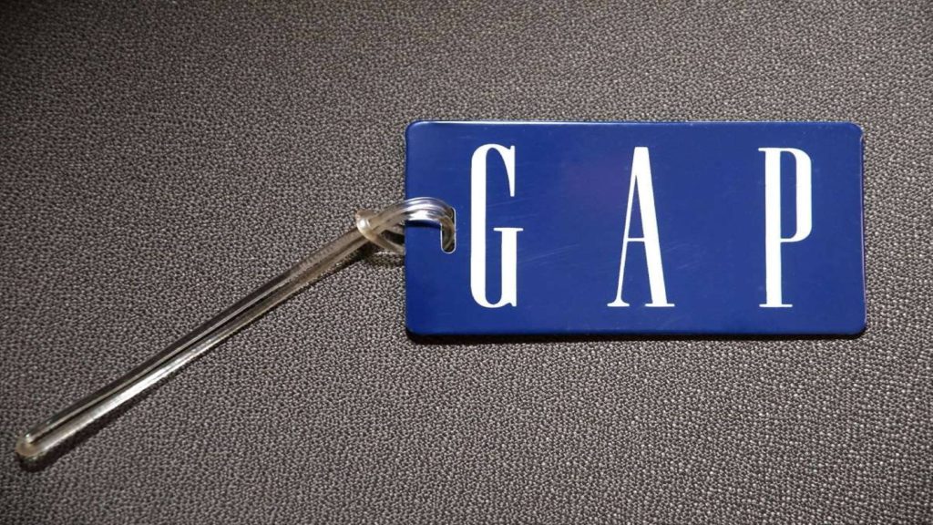 Close-up of navy blue Gap tag with white logo on grey textured background fashion wallpaper