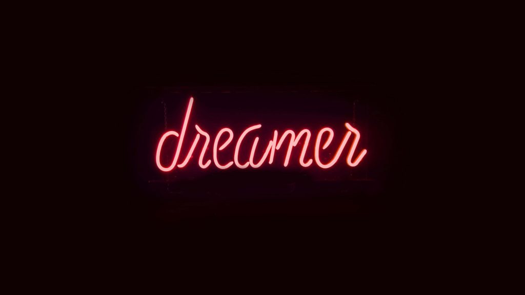 Minimalist neon dreamer wallpaper glowing red cursive on black background for 4K desktop