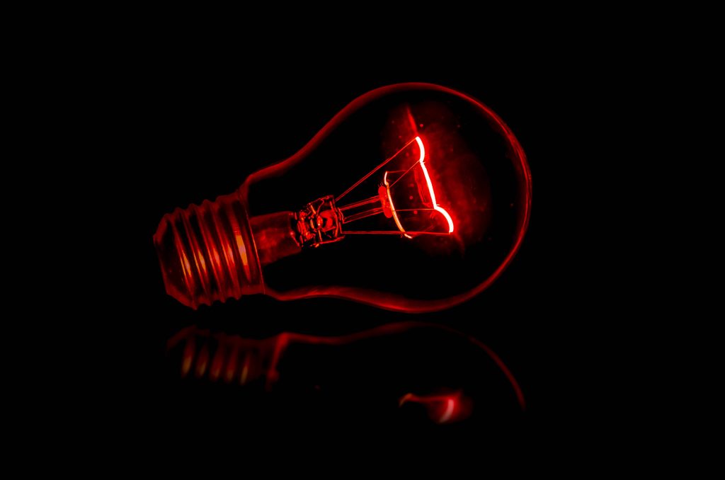Minimalist wallpaper glowing incandescent bulb with red filament on black background reflection