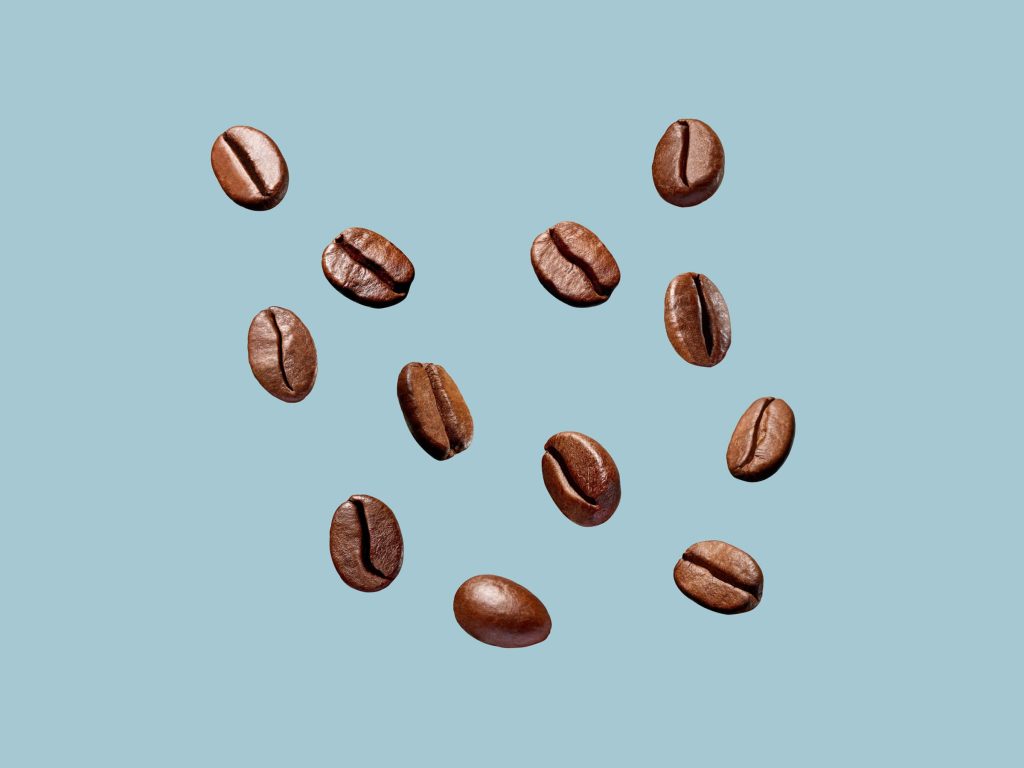 Minimalist wallpaper of roasted coffee beans on light blue background with bright studio lighting