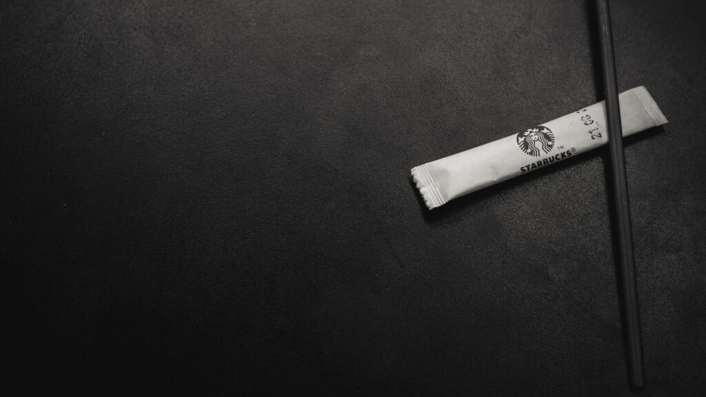 Minimalistic Starbucks wallpaper with single sugar packet and stir stick on dark textured background