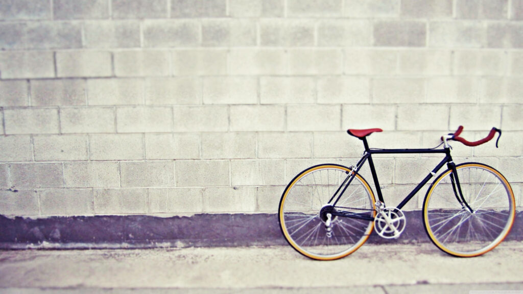 Sleek black bicycle with yellow rims against plain concrete wall minimalist urban background Wallpaper