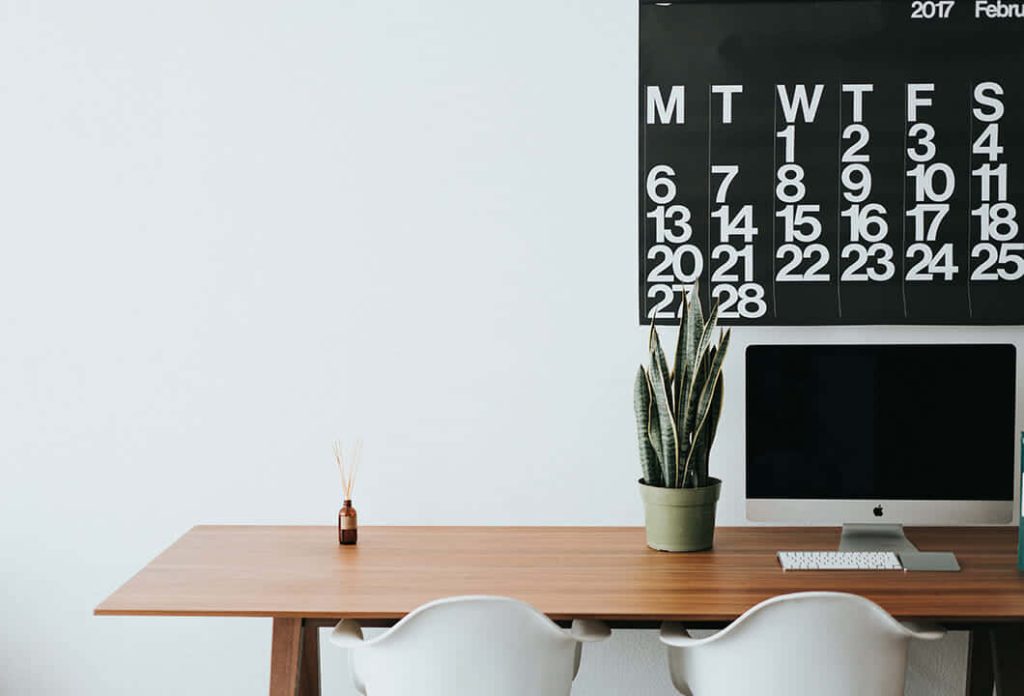 Minimalist home office Zoom wallpaper with wooden desk Apple computer snake plant 2017 calendar