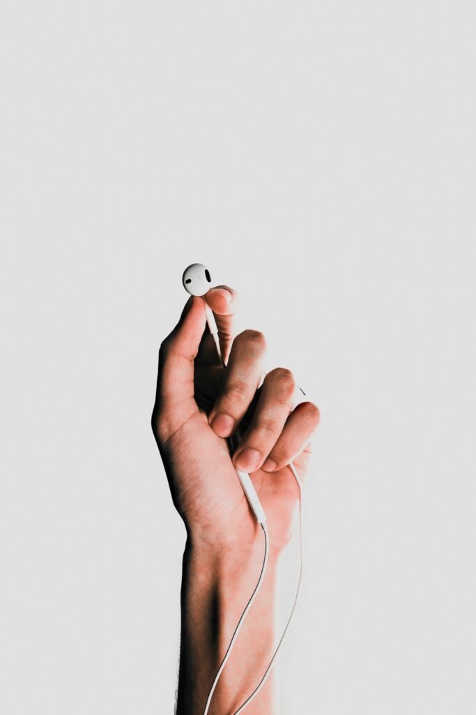 Minimalist Wallpaper: Hand Holding White Earbud on Clean Background