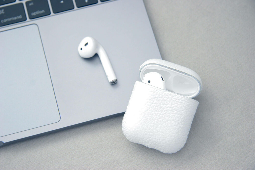Close-up of white AirPods case with one AirPod beside sleek MacBook laptop modern tech wallpaper