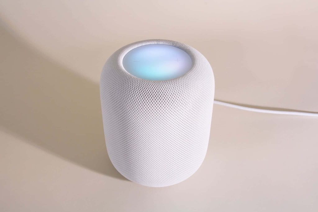 Minimalist white Apple HomePod with mesh texture and glowing top on warm neutral background Wallpaper