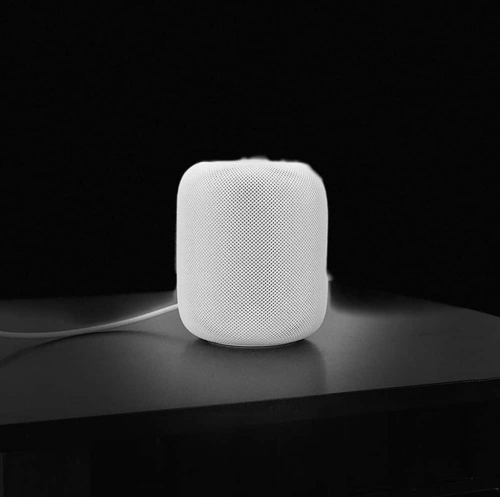 Minimalist white Apple HomePod on dark surface with dramatic lighting and textured mesh design Wallpaper