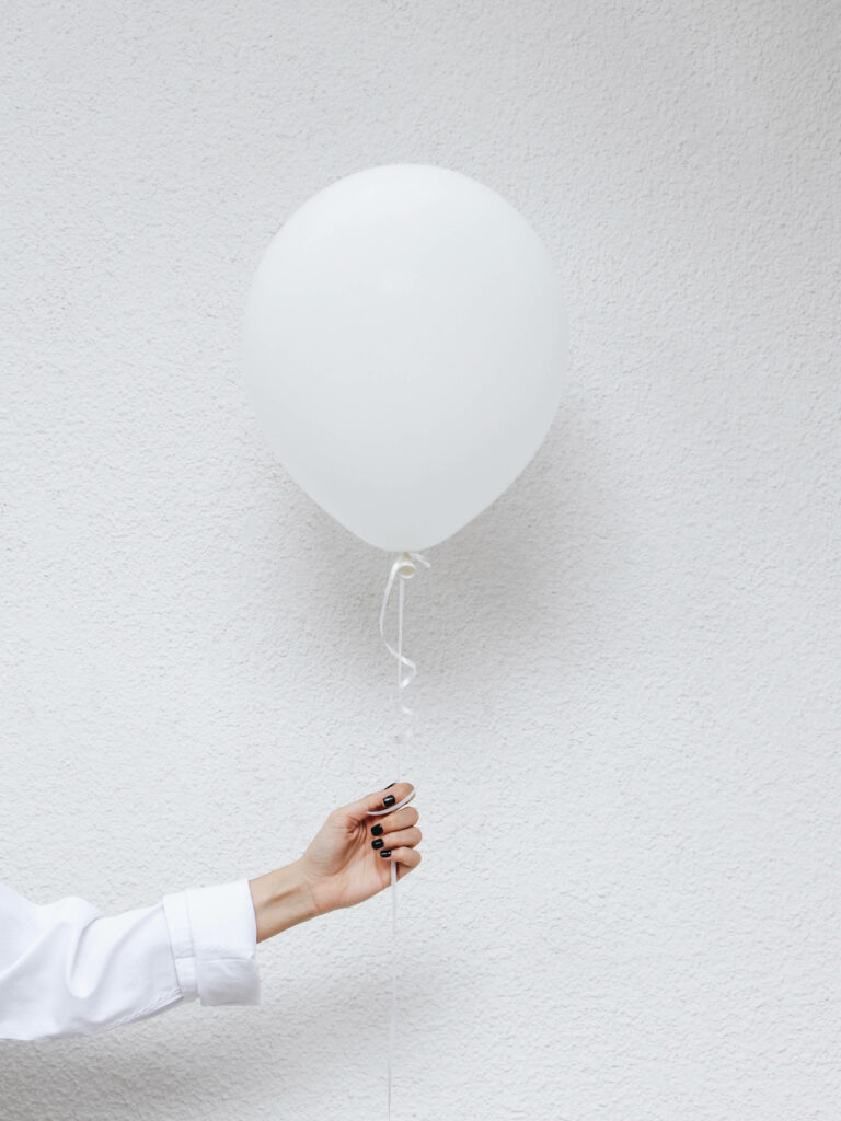 Minimalist white wallpaper with hand holding single white balloon on textured white background
