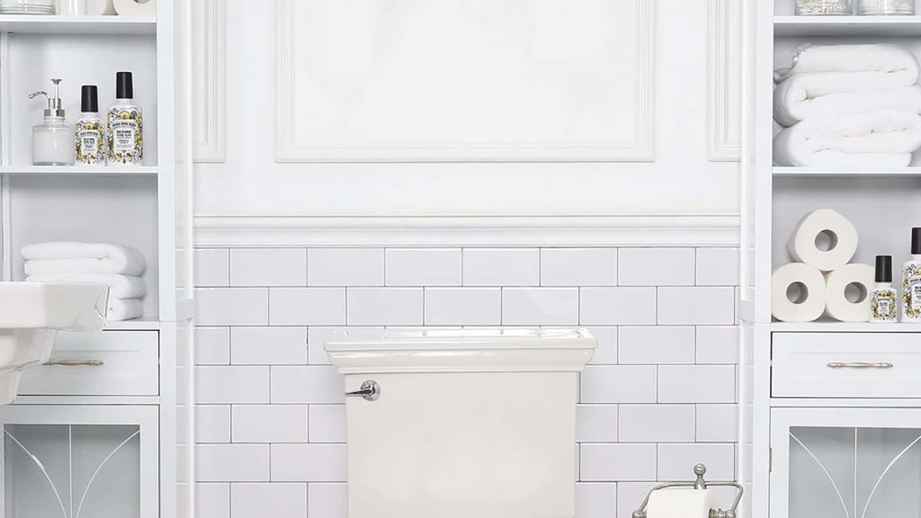 Bright clean bathroom with white toilet and subway tile walls flanked by storage cabinets and towels Wallpaper