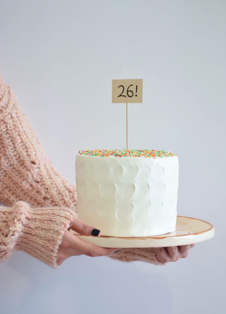 Minimalist white cake with colorful sprinkles and number 26 sign on soft neutral background Wallpaper