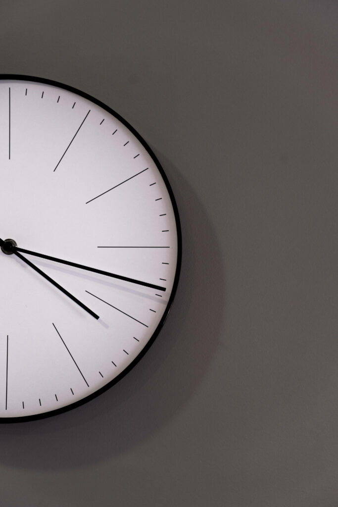 Minimalist white clock with thin black hands on smooth gray wall modern simple wallpaper background