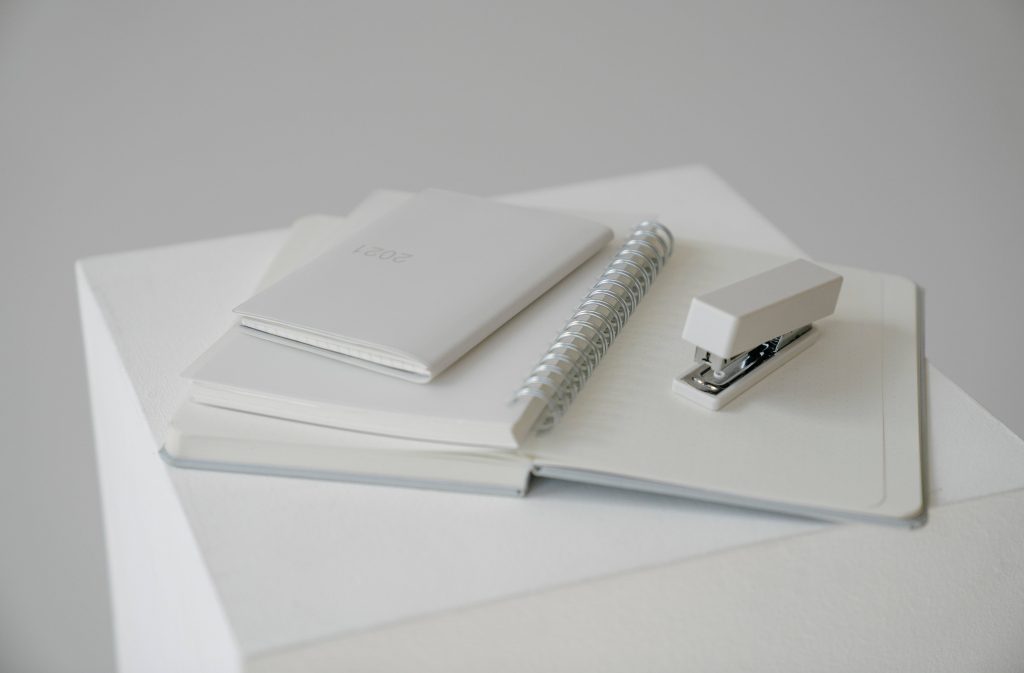 Minimalist white stationery wallpaper with open notebook planner and stapler on white desk