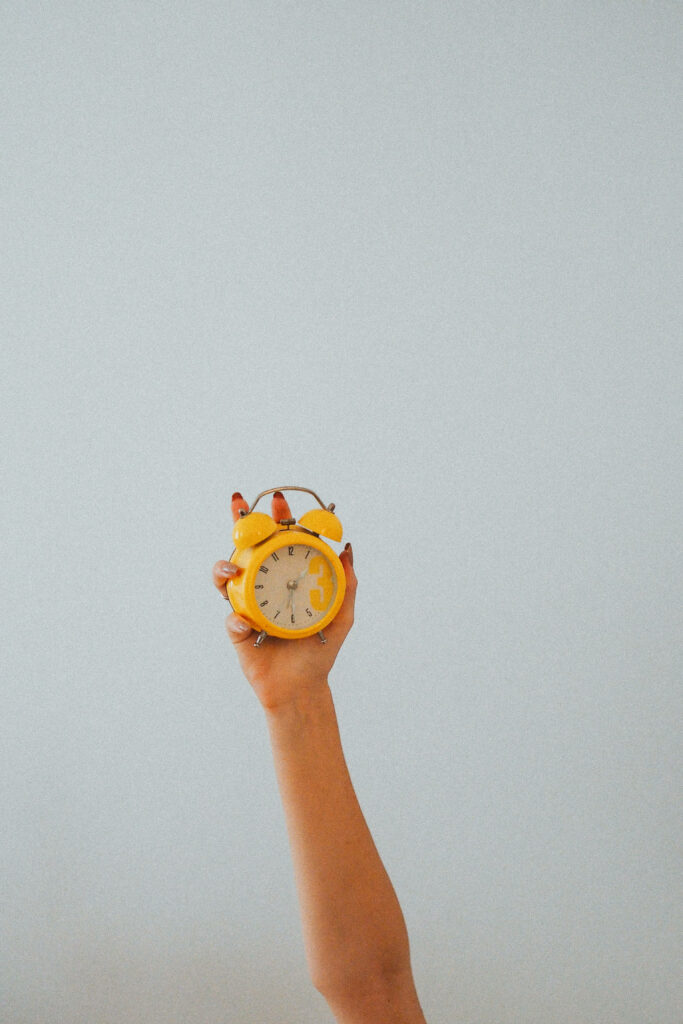 Minimalist wallpaper hand holding bright yellow alarm clock on light background focused on time