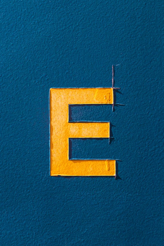 Minimalist bright yellow letter E on textured matte blue wall with distressed bold edges wallpaper
