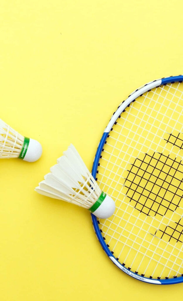 Graceful Badminton Composition with Blue and Gray Racket, Feathered Shuttlecocks, and Pastel Yellow Backdrop Wallpaper