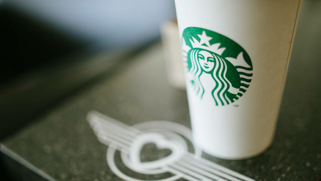 Minimalistic close-up of classic Starbucks coffee cup with green siren logo blurred café background Wallpaper