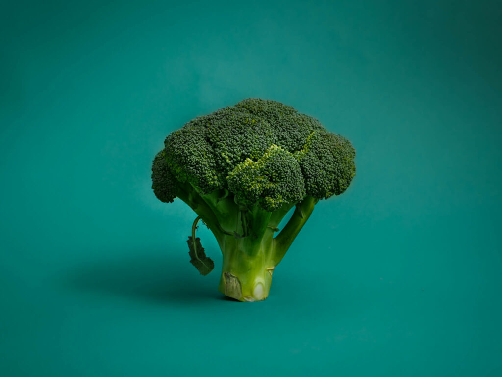 Minimalistic vibrant green broccoli floret on smooth teal background healthy food wallpaper