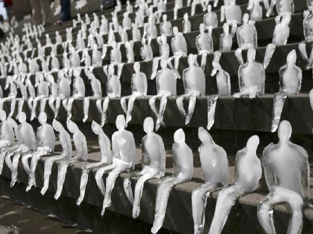 Rows of melting translucent ice people on stone steps representing climate change art installation Wallpaper