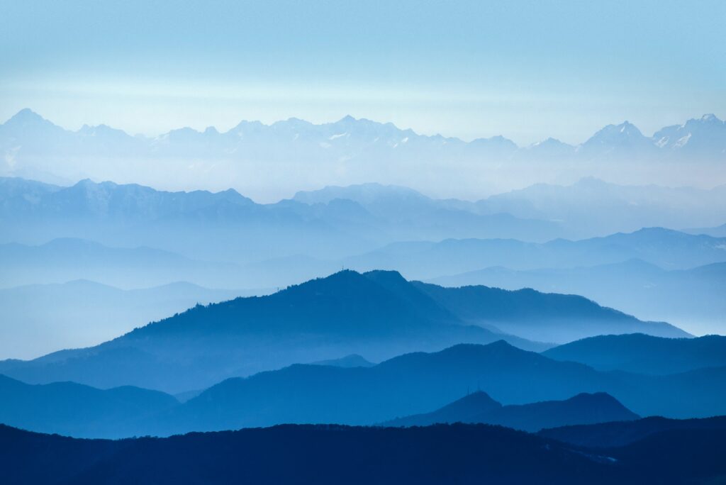 Serene blue layered mountains in mist with pale sky minimalist nature wallpaper background