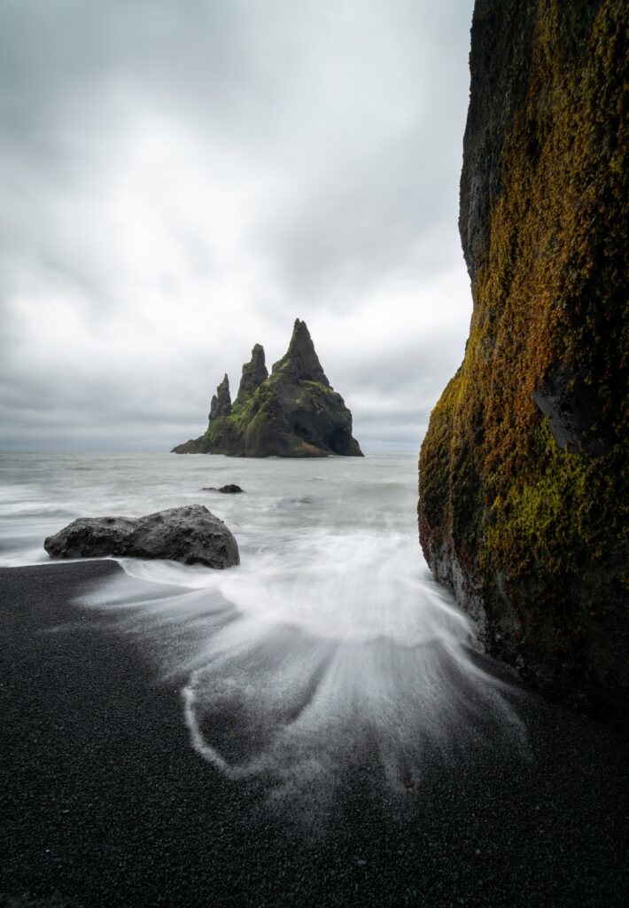 Misty coastal scene with rugged rocks mossy cliffs and black sand under overcast sky wallpaper