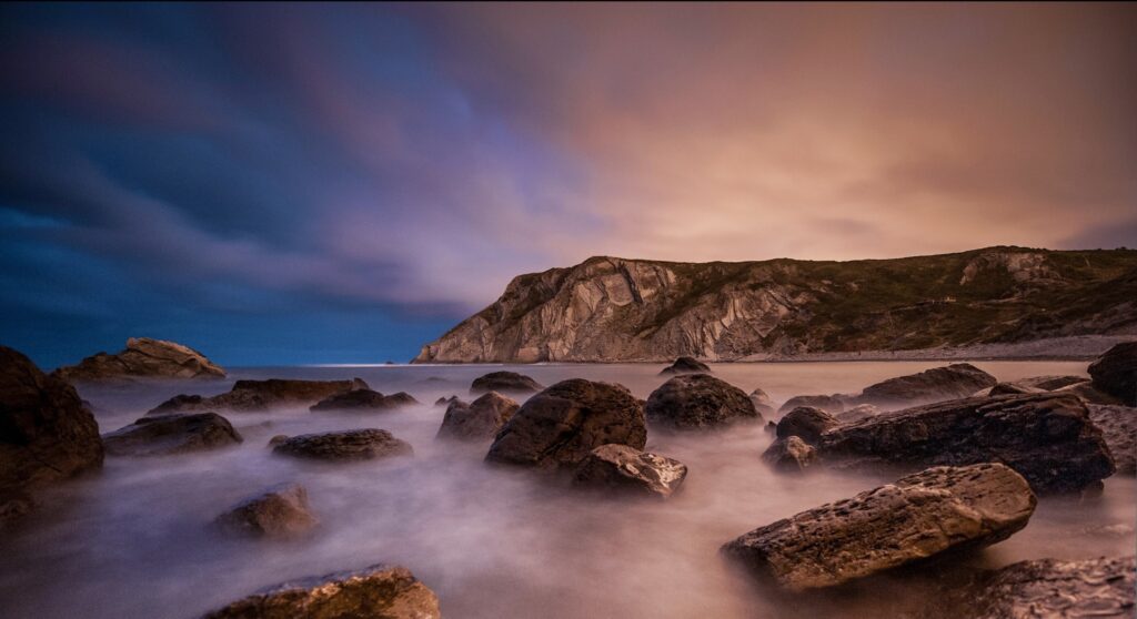 Misty coastal shoreline with rugged rocks and dramatic cliffs at vibrant dusk sky wallpaper background