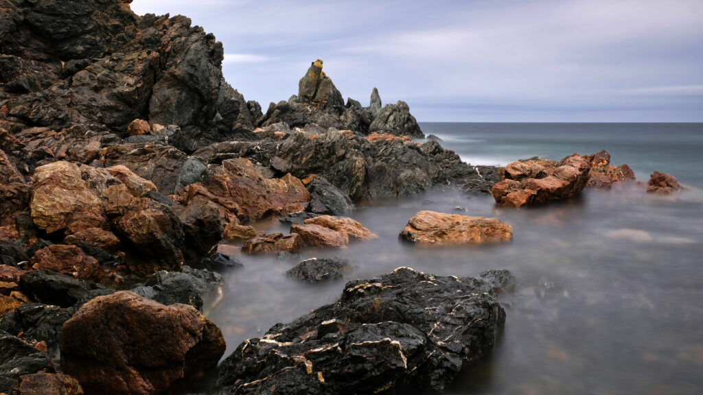 Serene coastal wallpaper with misty fog over rugged rocks and calm sea under cloudy sky