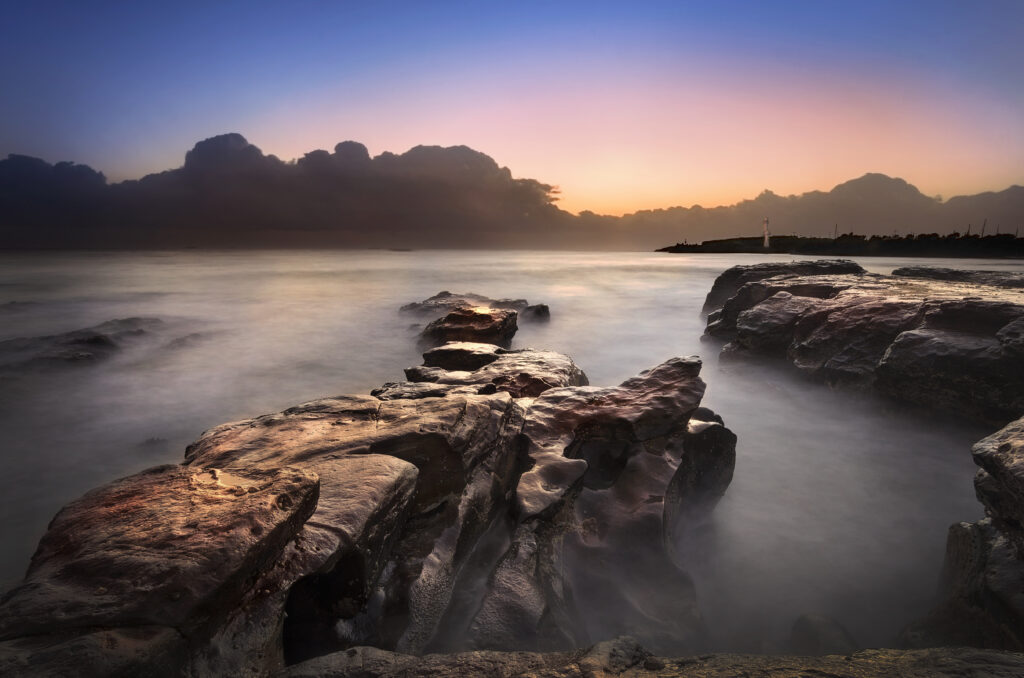 Foggy dusk landscape with rugged stones over calm water and soft gradient sky wallpaper background