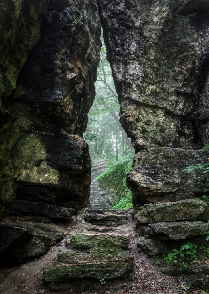 Natural stone gateway over misty forest gorge with lush greenery and soft fog wallpaper background