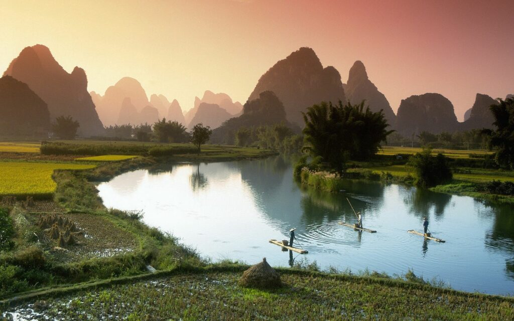 Misty morning in rural Vietnam with fishermen on boats amid green fields and limestone mountains Wallpaper
