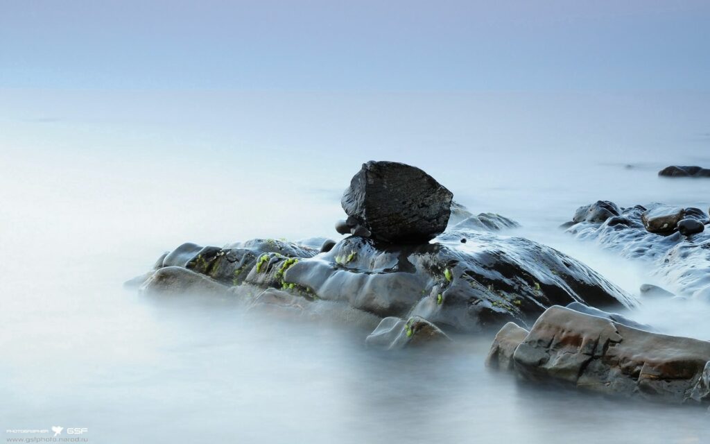 Serene moss-covered rocks in misty fog with soft light reflecting wet stones calm wallpaper background