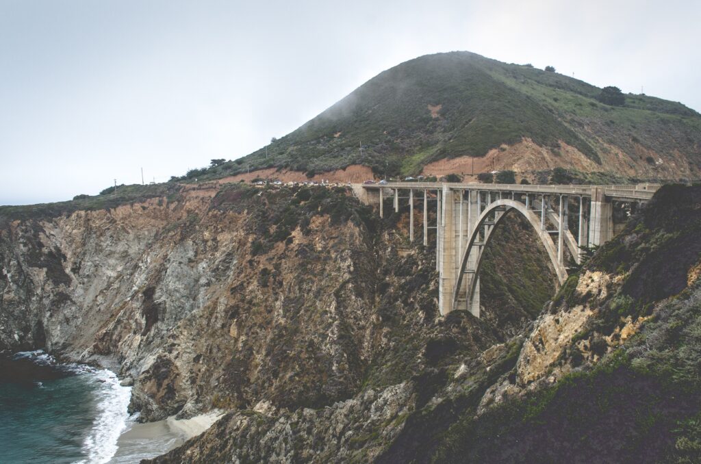 Arched bridge over rugged coastal cliffs with misty mountains background wallpaper view