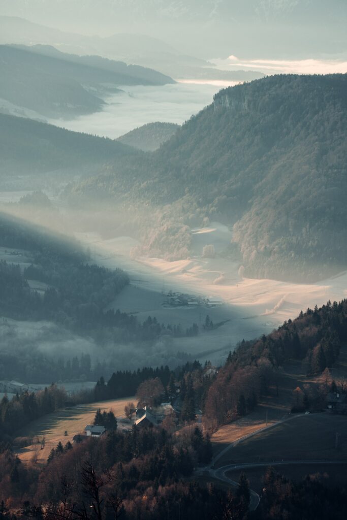 Aerial view of misty mountains with rolling hills foggy valleys soft sunlight and cozy houses Wallpaper