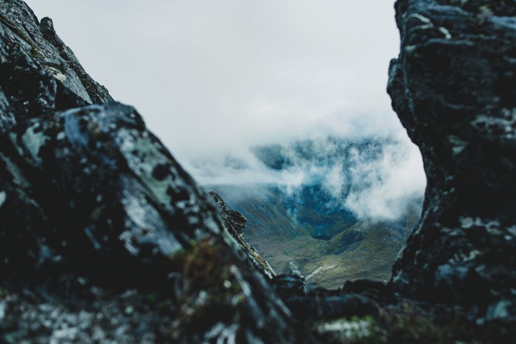 Dramatic mountain landscape with rugged rocks and swirling fog in misty blue green tones wallpaper