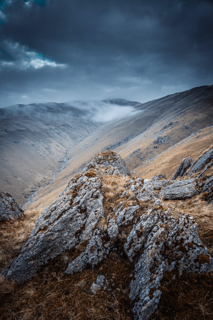 Rugged rocks and misty mountain slopes under dramatic clouds in a serene landscape wallpaper