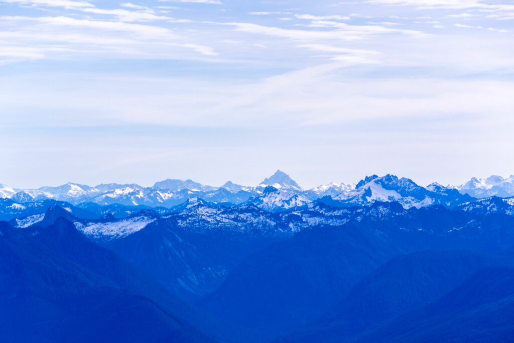 Serene blue mountain landscape with misty fog snow-capped peaks and cloudy sky wallpaper background