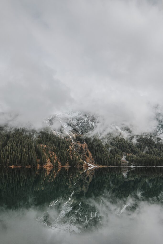 Serene misty mountains with pine forests and calm lake reflecting dramatic clouds wallpaper background