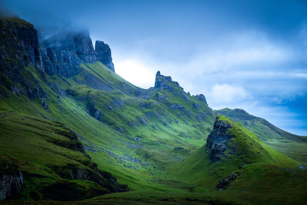Dramatic misty landscape with steep green slopes and rugged rock formations in blue sky Wallpaper