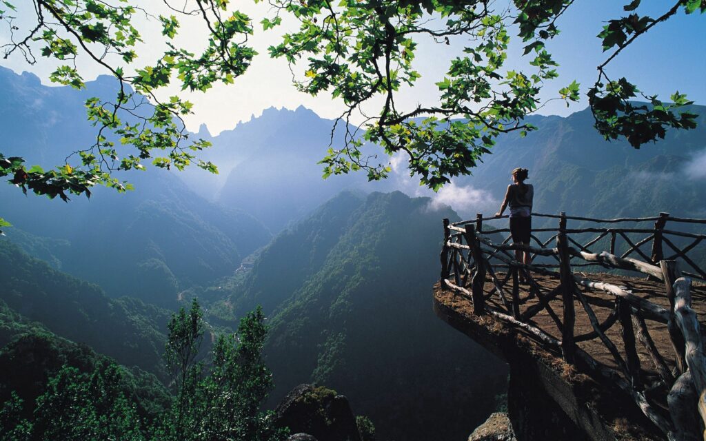 Person on wooden balcony overlooking misty green mountain peaks and lush valley landscape wallpaper