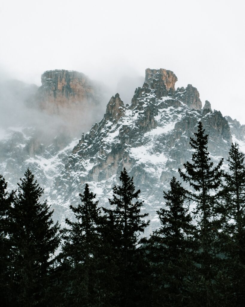 Dramatic mountain peak above snow dusted pine trees shrouded in mist and low clouds Wallpaper