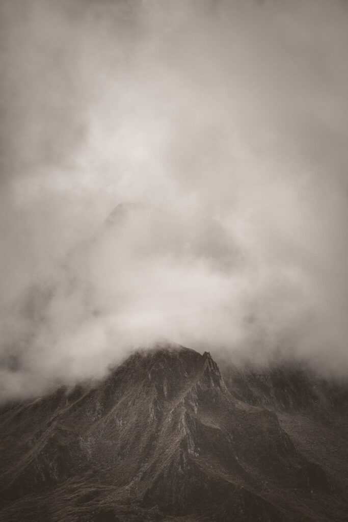 Dramatic mountain peak emerging through swirling clouds and fog in tranquil earthy tones wallpaper