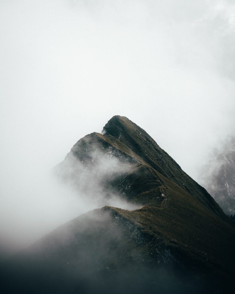 Dramatic mountain wallpaper with jagged peaks and swirling fog over misty slopes in muted tones