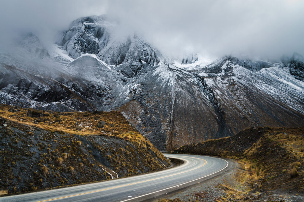 Winding mountain road through foggy rugged peaks with snowy rocky slopes and muted earth tones Wallpaper
