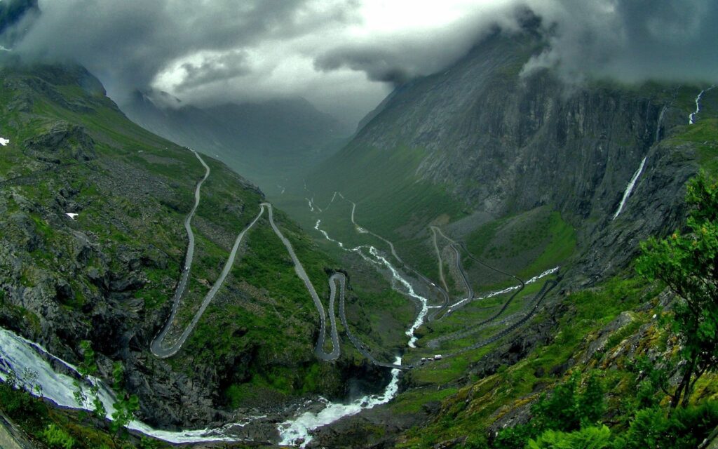 Dramatic mountain landscape with winding cliff roads misty clouds and lush green valleys wallpaper